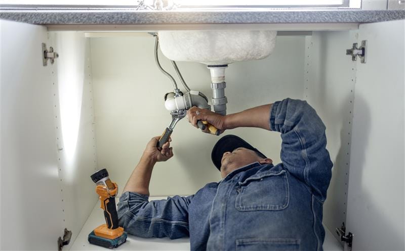 Plumber repairing pipes beneath a bathroom sink in Sebastian