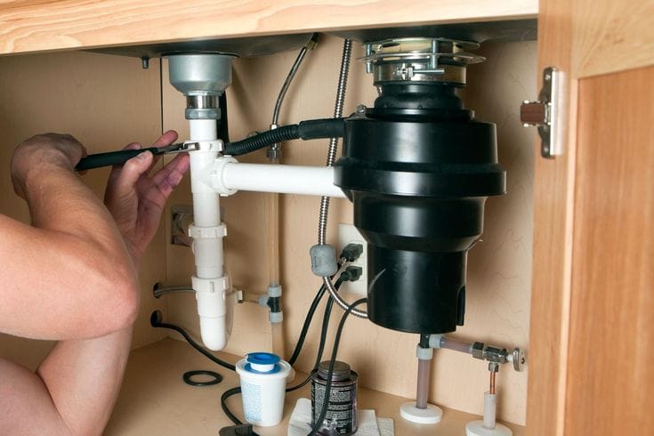 Plumber installing a garbage disposal beneath a kitchen sink in Sebastian