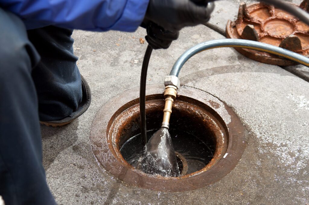 Plumber hydro jetting a sewer line through a manhole in Sebastian