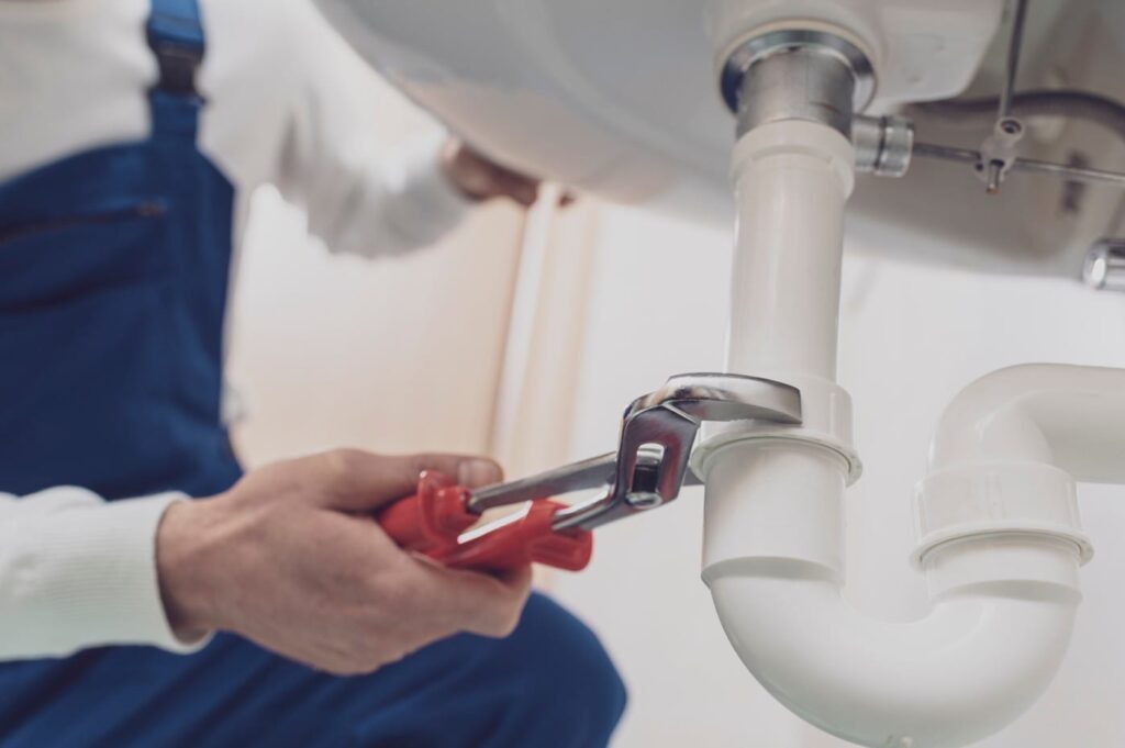 Plumber repairing a white drain pipe beneath a sink in Sebastian