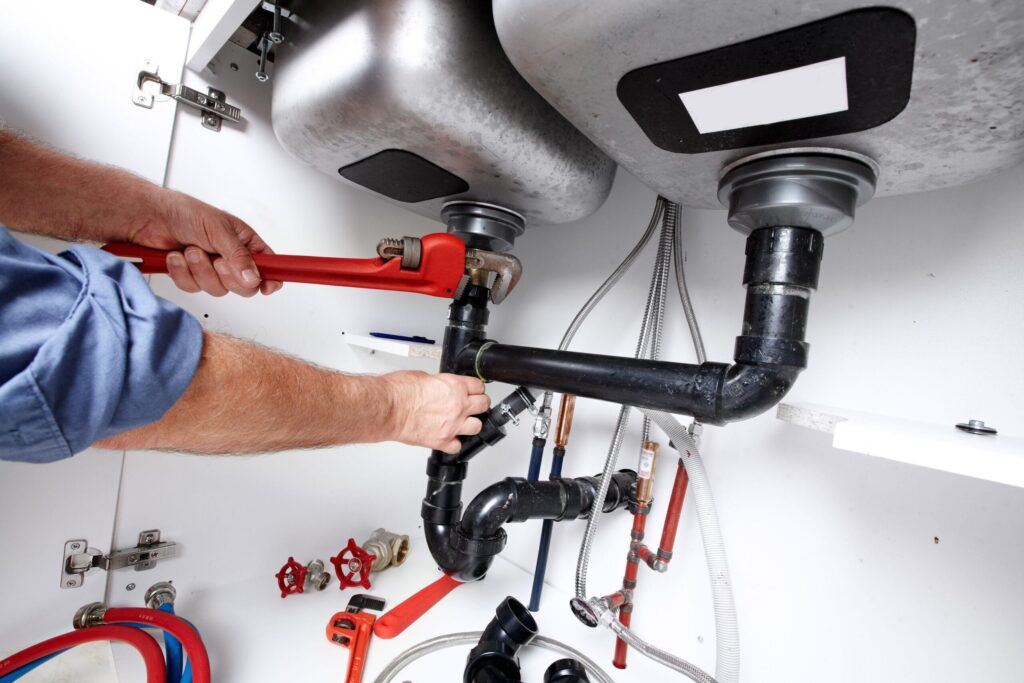 Plumber repairing drain pipes beneath a kitchen sink in Sebastian